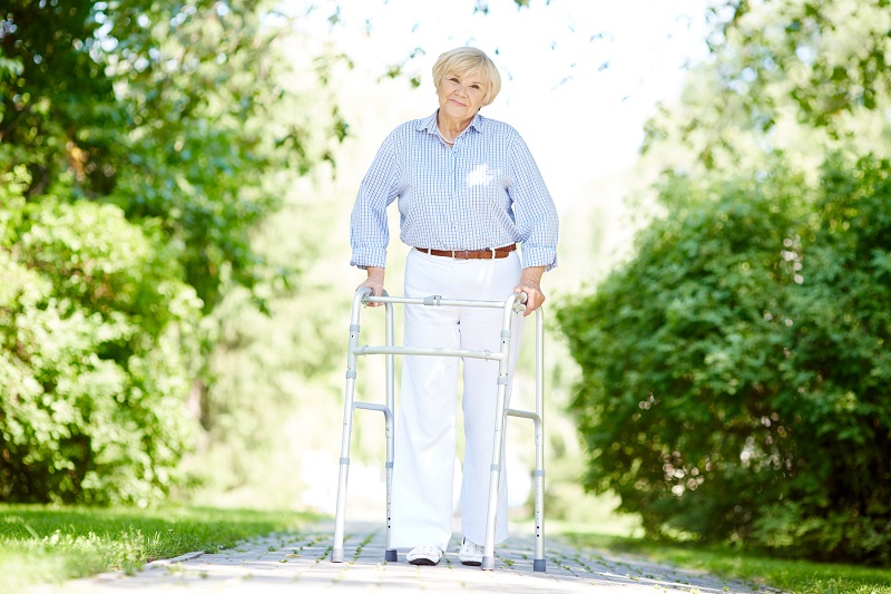 Image d'une femme âgée se promenant dans un parc avec un déambulateur